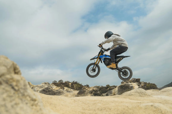 Rider airborne on a Zonveer DX1 dirt e-bike over a sandy landscape